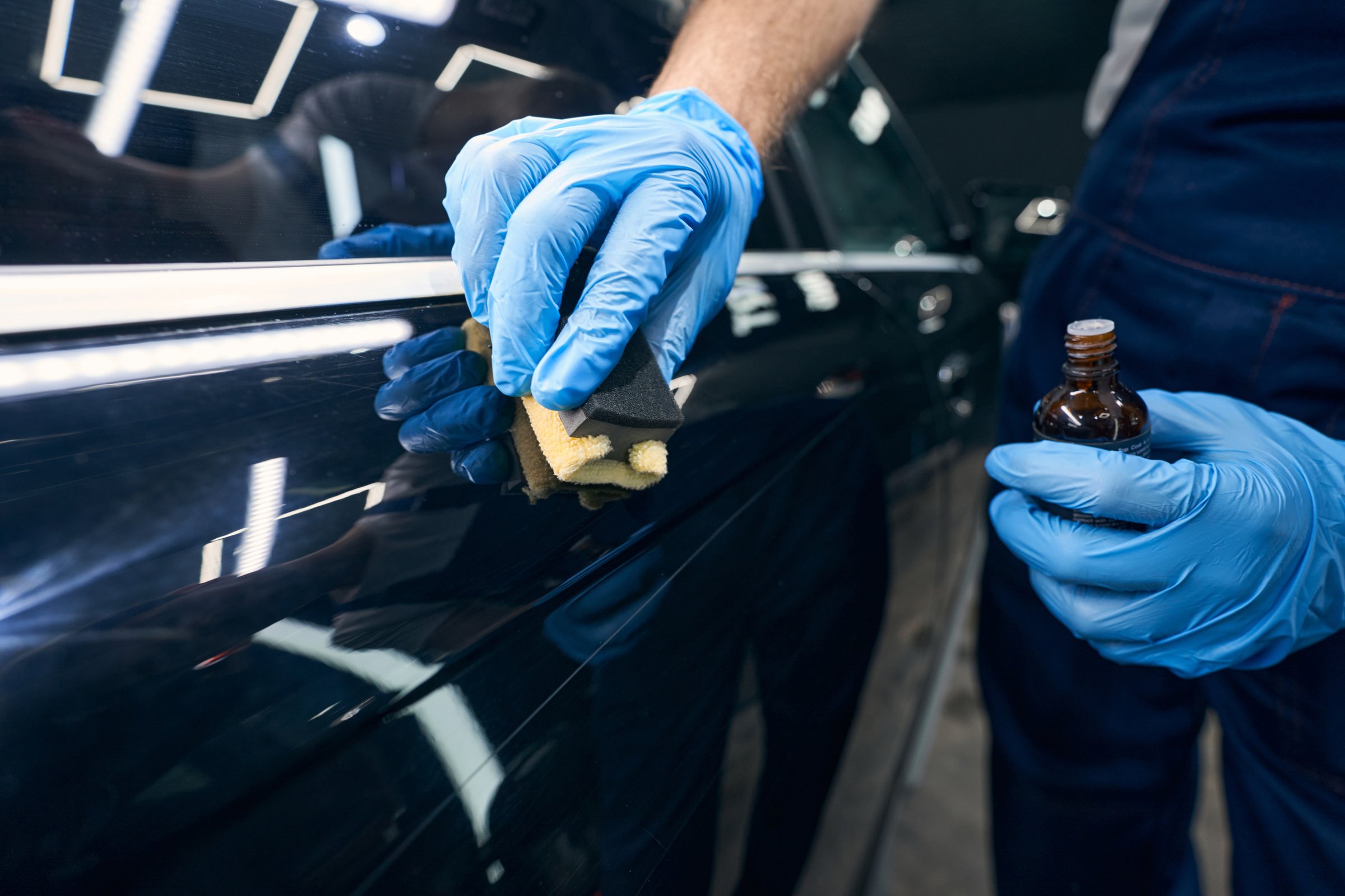 Worker with microfiber applicator spreading ceramic coating on car